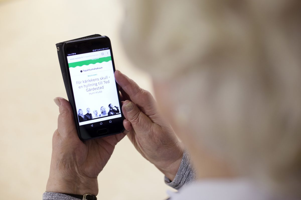 Seniori pitää älypuhelinta kädessään, jossa on Helsingin kaupungin tapahtumahaku auki.