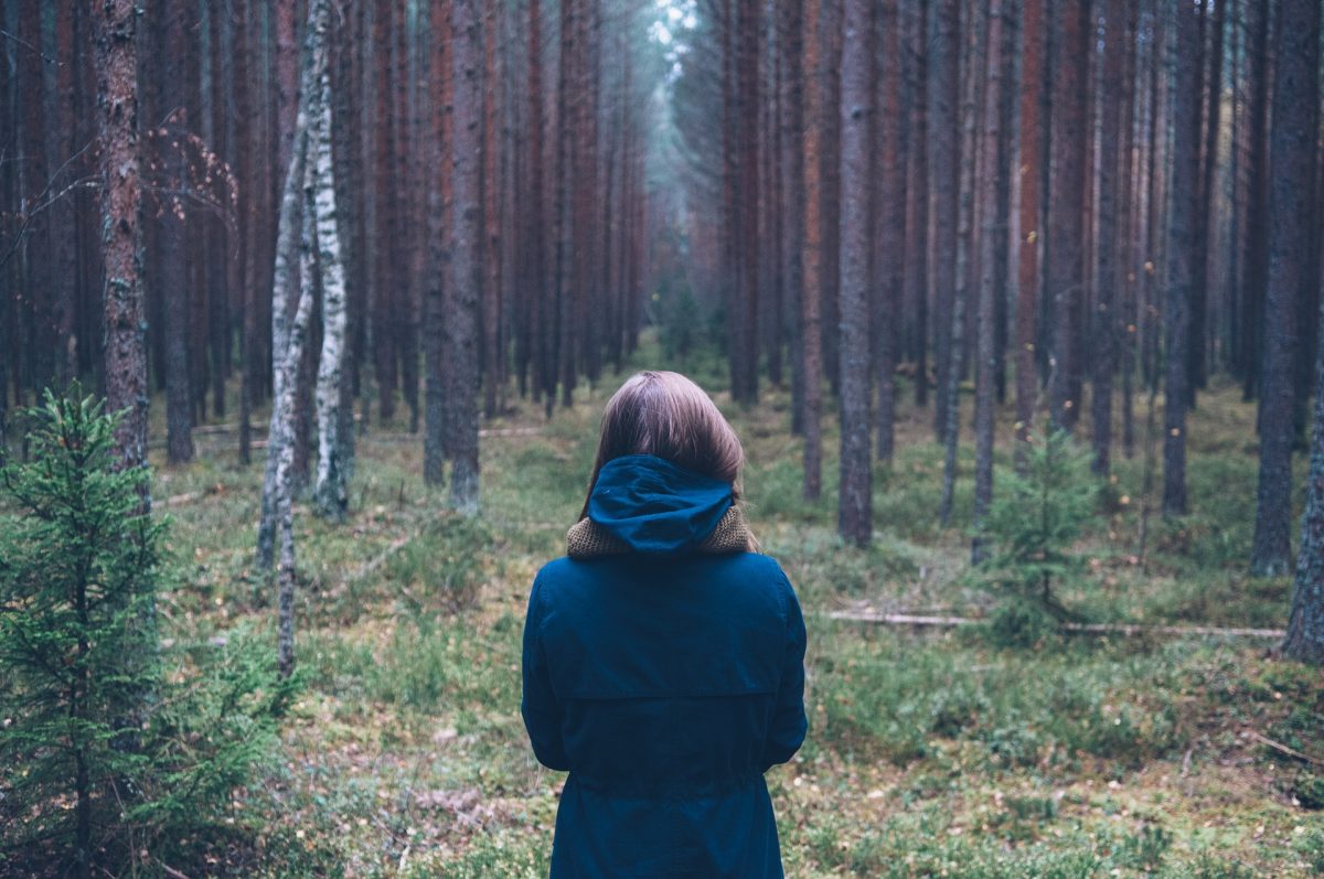 Nainen seisoo syksyisessä metsässä selkä kameraan päin.